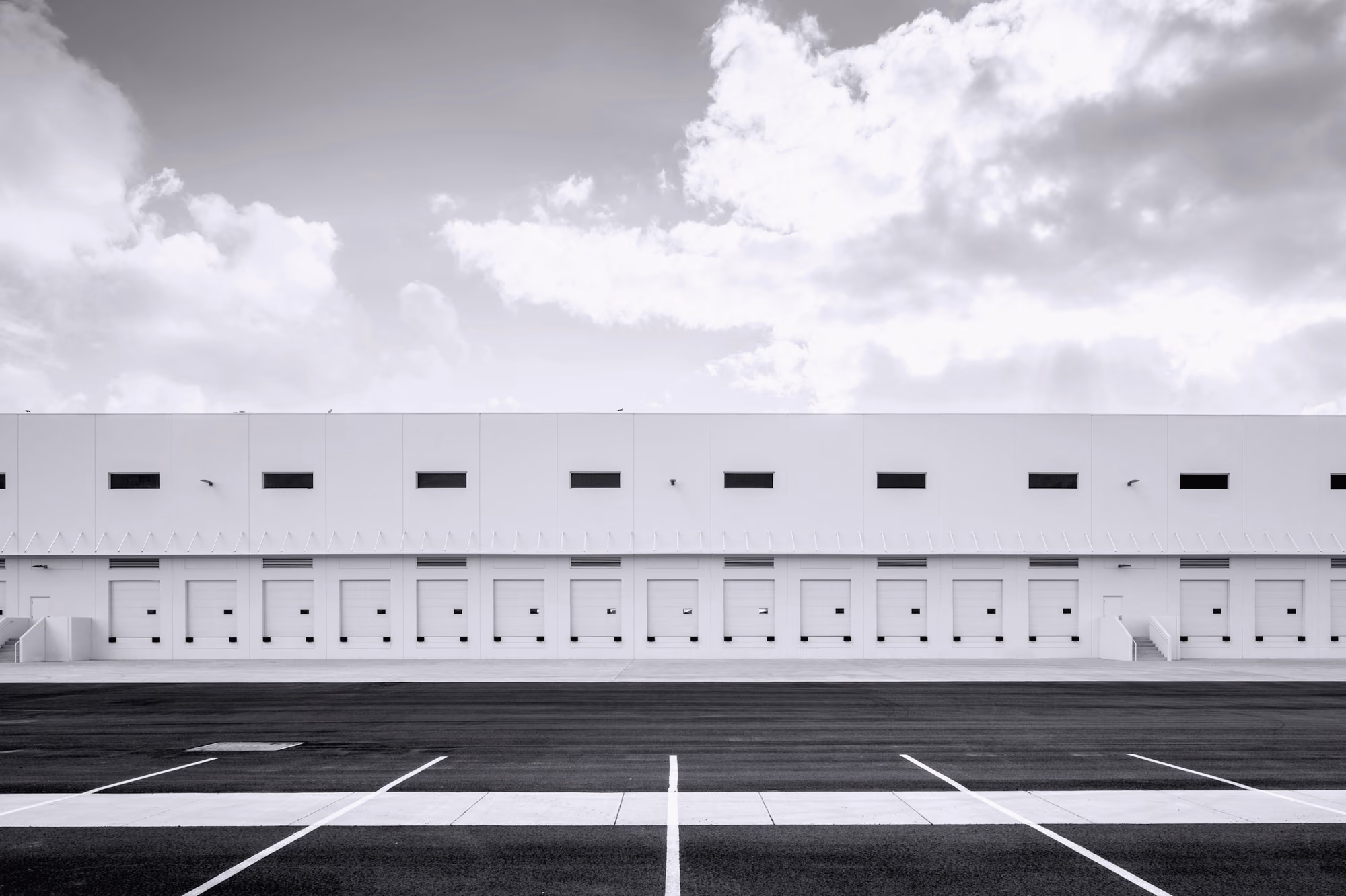 Edificio industrial largo y bajo, blanco, con ventanas pequeñas y cielo con nubes