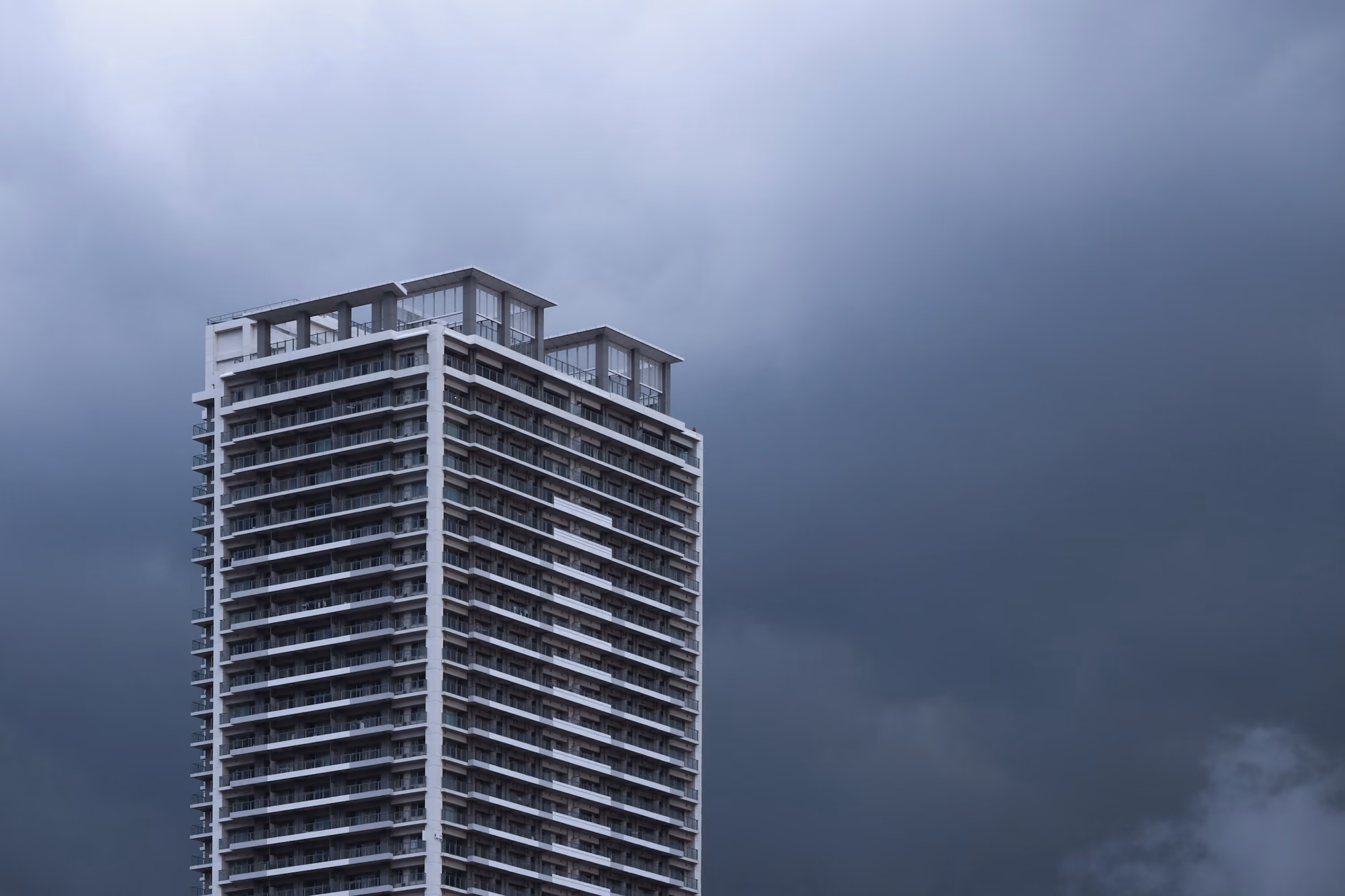 Torre residencial de muchos pisos contra un cielo azul oscuro y nublado